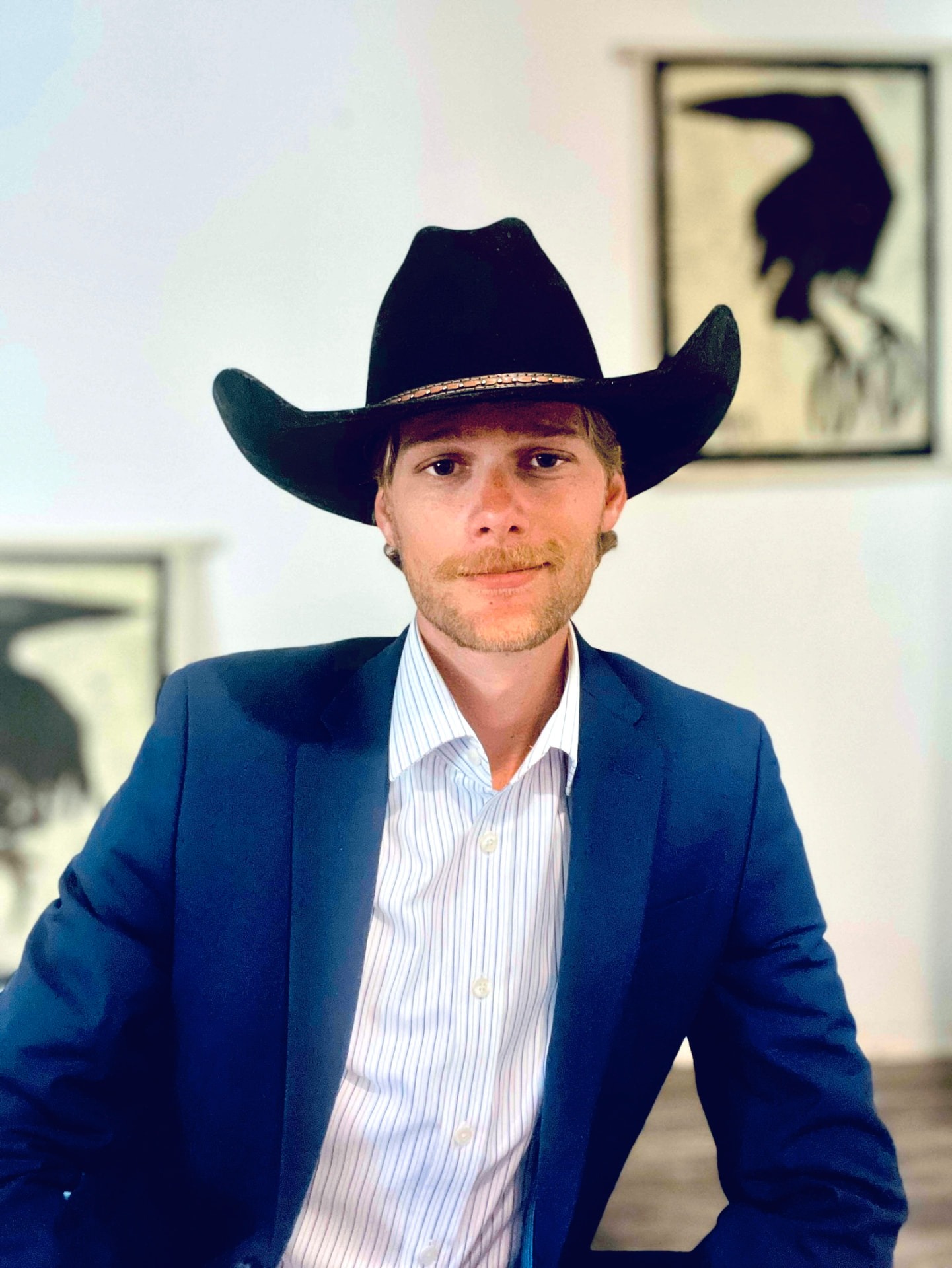 Brock Skinner in a navy blazer, striped shirt, and black cowboy hat